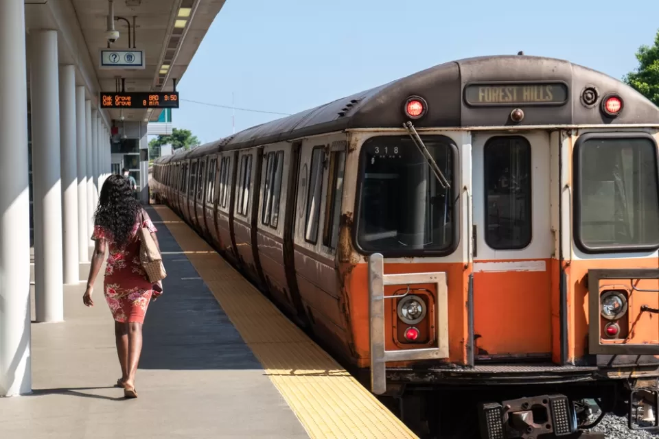 Orange Line train pulling into station with one woman waiting to board in Boston, Massachusetts